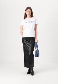 White t-shirt with black text, paired with a black leather skirt. She holds a blue crossbody bag and wears black ankle boots.