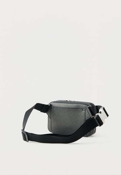 Μικρή μαύρη τσάντα χιαστί με υφή, ρυθμιζόμενο φαρδύ λουρί και ασημένια αγκράφα, τοποθετημένη σε απλό λευκό φόντο.