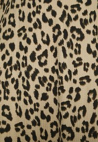 Tecido bege com uma superfície texturizada apresentando um padrão de estampa de leopardo preto. As manchas variam em tamanho e forma ao longo do material.