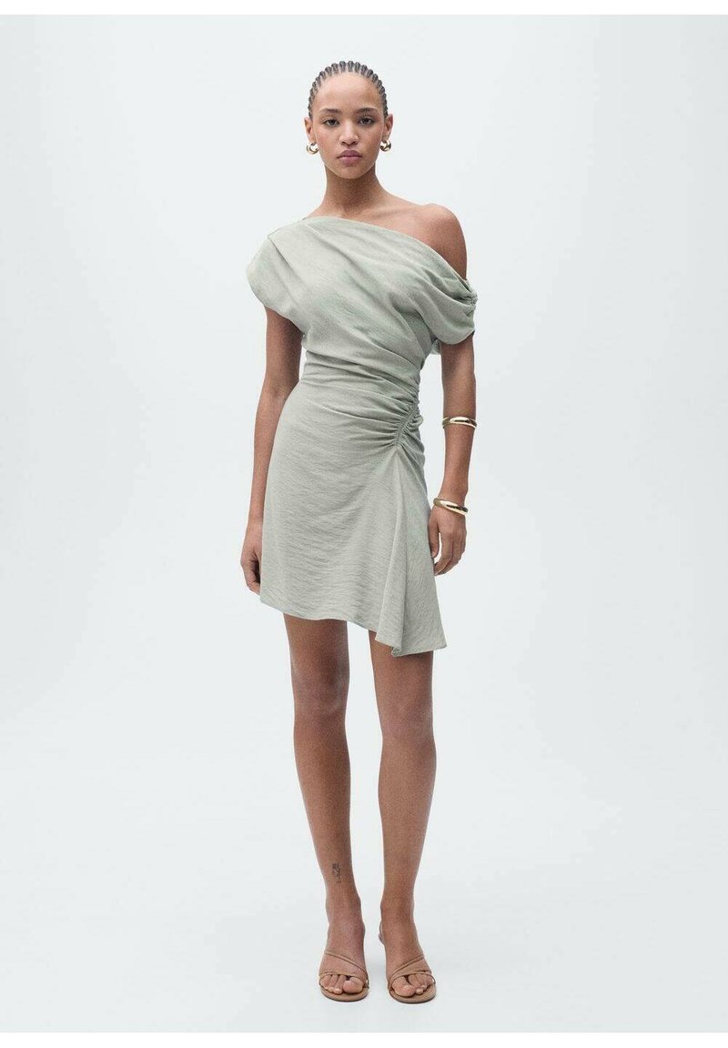 Off-shoulder, light green dress with draped fabric, side ruching, asymmetrical hem, and smooth texture. Worn with simple sandals and accessories.