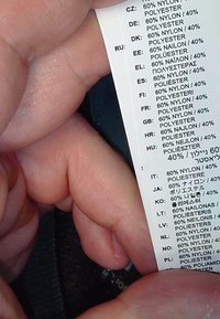 Mano sosteniendo una etiqueta de ropa que muestra la composición del tejido como 60% nailon y 40% poliéster en varios idiomas.