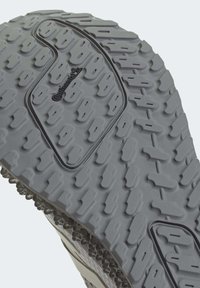 Suela de zapato de goma gris con un patrón de banda de rodadura distintivo, que presenta surcos y detalles texturizados. Incluye el logotipo en el centro.