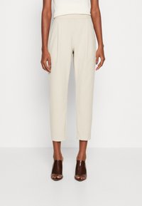 Beiga högmidjade byxor med veck, knälånga och med sidofickor. Slät tyg med en vacker passform. Bärs tillsammans med bruna öppna klackar.