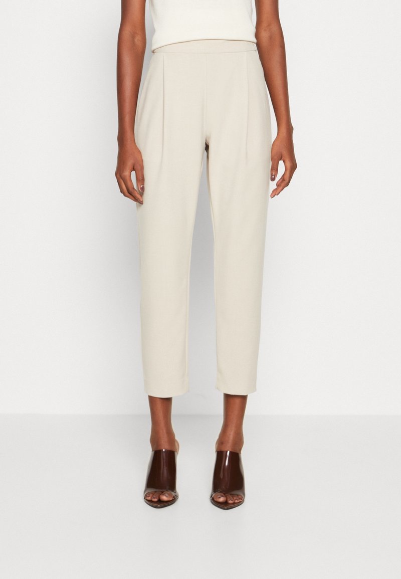 Beiga högmidjade byxor med veck, knälånga och med sidofickor. Slät tyg med en vacker passform. Bärs tillsammans med bruna öppna klackar.