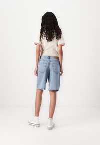 Denim shorts in light blue with a relaxed fit, featuring a mid-rise waist and two back pockets. Paired with a white, short-sleeve top.