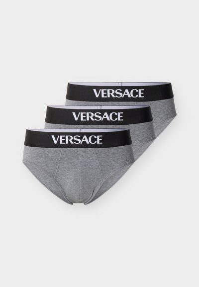 Trois slips pour hommes gris empilés, chacun avec une ceinture noire arborant le logo blanc "VERSACE" centré à l'avant.