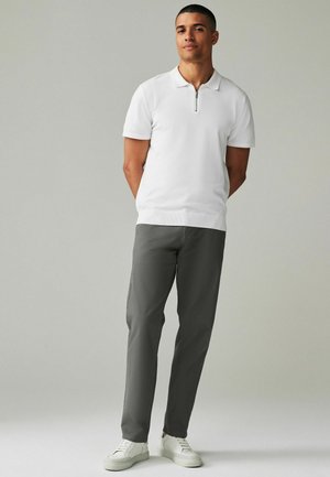 Hvid polo skjorte med kort lynlås ved halsen, parret med grå bukser og hvide sneakers. Glat stofstruktur, skræddersyet design.