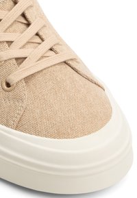 Baskets en toile beige avec lacets assortis et semelle en caoutchouc crème, montrant un gros plan de la pointe et de la zone des lacets.