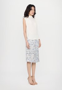 Hvit ermeløs topp med høy hals, sammen med et blomstrete kne-length skjørt i blå og kremtoner, komplettert med beige hælsandaler.