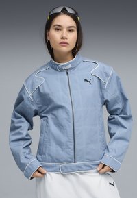 Lichtblauwe jas met een gestikt patroon, hoge kraag en witte bies. Voorzien van een ritssluiting aan de voorkant en een Puma-logo op de borst.