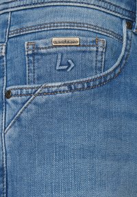 Jasnoniebieskie dżinsy z fakturowanej tkaniny. Posiadają małą tylnią kieszeń z metalową metką z napisem "LANCERTO" oraz kontrastowe szwy.