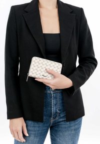Light-colored zippered wallet with a geometric pattern, held in hand, paired with a black blazer and blue jeans.