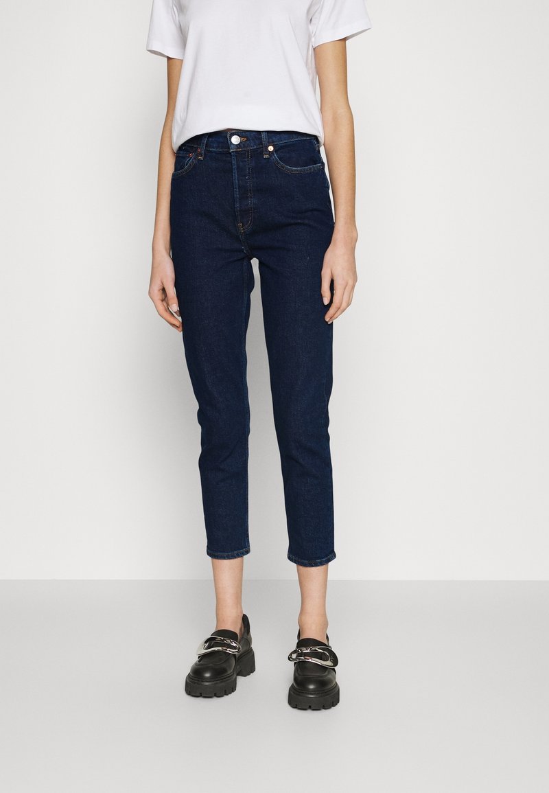 Mörkblå cropped jeans i denimtyg, med en figursydd silhuett, framfickor och en klassisk knäppning i midjan.