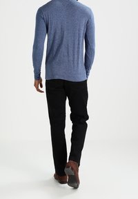 Blå långärmad skjorta med en texturerad yta, kombinerad med svarta byxor. Bruna skor med en slät yta. Utsikt från baksidan.