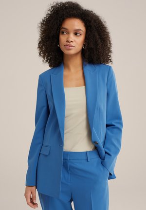 Blue tailored blazer with sharp lapels, single button closure, and two front pockets, worn over a light beige top. Smooth fabric, sleek design.