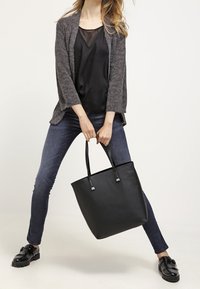 Mustapohjainen laukku kahdella olkahihnalla ja metallisilla yksityiskohdilla, valmistettu sileästä nahasta. Laukku on suorakulmainen muotoilultaan ja minimalistinen.