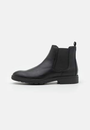 Botte Chelsea en cuir noir avec panneaux élastiques sur les côtés, languette au talon, talon bas et semelle en caoutchouc texturée.