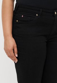 Jean en denim noir au design ajusté. Comprend une petite poche rehaussée d'une bande rouge, blanche et bleue ainsi que de quincaillerie dorée.