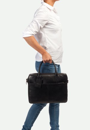 Malette en cuir noir avec poignées doubles, poche avant et étiquette de bagages. Texture lisse et forme rectangulaire, idéale pour un usage professionnel.