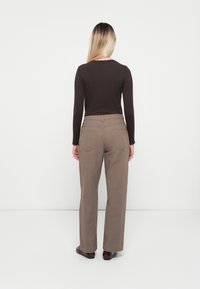 Brun langermet topp med bølget hals, kombinert med lysebrune bukser med rett bein. Jevn tekstur på stoffet gjennom hele.
