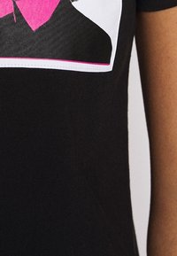 Maglietta nera con una grafica di una persona che indossa un maglione rosa sopra una maglietta nera, contornata di bianco con un bordo rosa.