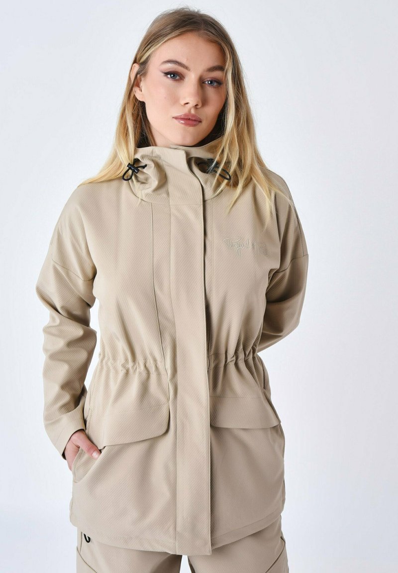 Beige vandtæt jakke med en tekstureret overflade, justerbar hætte, elastisk talje og to frontlommer; minimalistisk design uden synlig branding.