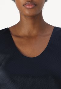 Navyblaues Struktur-Oberteil mit weitem Ausschnitt und dezenten Mustern. Hergestellt aus einem leichten, atmungsaktiven Stoff.