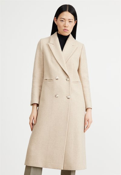 Beige kaksirivi takki, jossa on muotonsa mukautettu design, viistetyt kaulukset, kaksi etupuolta taskua ja nappikoristeet. Karheaa villakangasta.