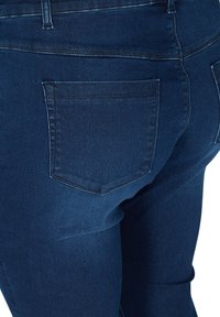 Los jeans de mezclilla azul oscuro presentan un diseño ajustado con una textura suave. Hay dos bolsillos traseros con costuras sutiles.