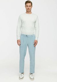 Hellblaue Cordhosen mit tailliertem Schnitt, gefältelter Vorderseite und flachem Bund, kombiniert mit einem figurbetonten weißen Langarmhemd.