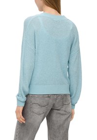 Jasnoniebieski sweter dzianinowy z ribbowanym wykończeniem i obszernymi rękawami, z fakturowanym wykończeniem i luźnym krojem. Noszony z szarymi dżinsami.