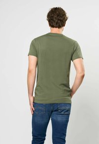 Olive spalvos trumpų rankovių marškinėliai, pagaminti iš minkštos medvilnės, prigludęs dizainas su apvalia kaklo iškirpte, derinami su mėlynomis džinsinėmis kelnėmis. Lygus paviršius, be raštų.