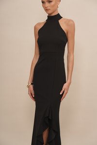 Crna halter haljina s prilagođenim tijelom i lepršavim volanom na rubu. Glatki, rastezljiv materijal s elegantnom siluetom. Nošeni zlatni dodaci.