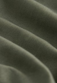 Groene stof met een gladde textuur, met subtiele diagonale lijnen en plooien die diepte en zachtheid creëren.