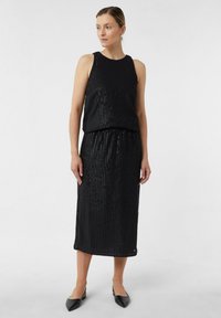 Zwarte mouwloze jurk met verticale gestreepte patroon, elastische tailleband, knie-lengte, subtiele glans, gecombineerd met zwarte puntige flats.