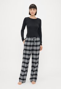 Langærmet sort skjorte parret med løst siddende sort-hvid ternede pyjamasbukser, der har elastisk talje og sidelommer.