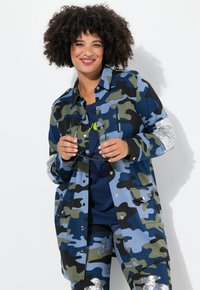 Chaqueta camuflada en tonos azules y verdes, con acentos plateados en las mangas, y un corte relajado con cierres de botón.