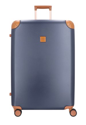 Valigia rigida blu navy con manici in pelle color cuoio e dettagli agli angoli, quattro ruote nere girevoli e manico retrattile esteso.