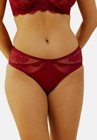 Culotte en dentelle et tulle bourgogne avec un motif floral sur la taille, ornée d'un petit nœud décoratif à l'avant et d'un tissu lisse.