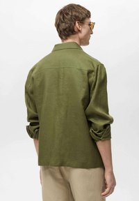 Olive green shirt with rolled sleeves, back yoke detail, and a relaxed fit. Made from lightweight fabric with a smooth texture.