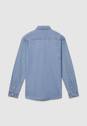 Chemise en denim bleu clair à manches longues, poignets boutonnés et col classique. Tissu texturé avec une finition lisse et des détails d'usure subtils.