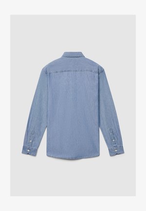 Chemise en denim bleu clair à manches longues, poignets boutonnés et col classique. Tissu texturé avec une finition lisse et des détails d'usure subtils.
