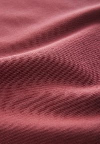 Tejido texturizado en un color rosa suave con una superficie lisa, mostrando sutiles ondulaciones y detalles de patrón tejido.