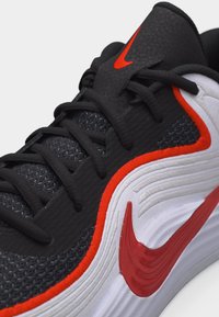 Fekete-fehér sportcipő piros kiemelésekkel, fekete fűzőkkel, texturált felsőrésszel, valamint piros Nike pipával az oldalán és a nyelvén.