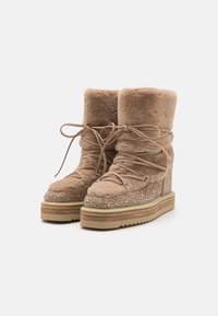 Botas de tobillo de piel sintética marrón con diseño de cordones, suela de cuña y adornadas con rhinestones transparentes a lo largo del borde inferior y del tacón.