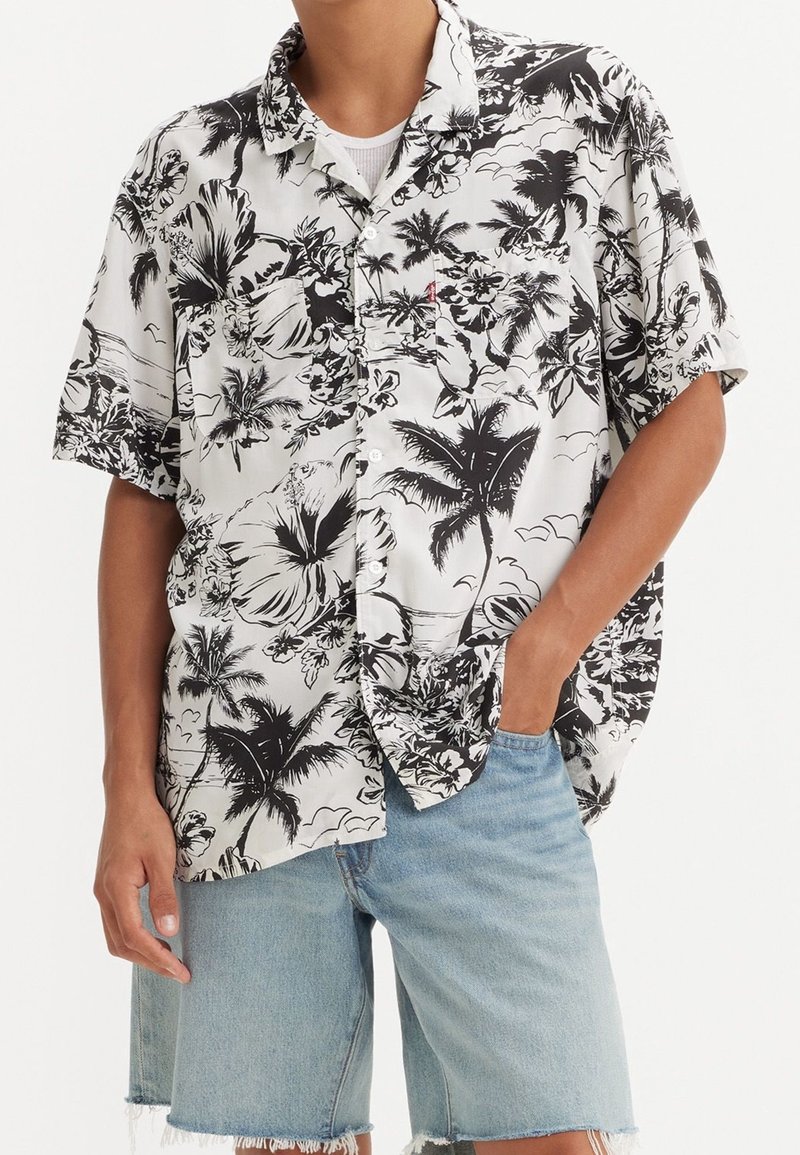 Camicia a maniche corte con un motivo floreale in bianco e nero, caratterizzata da palme e fiori di ibiscus, realizzata in tessuto leggero.