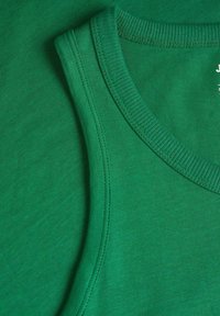 Canottiera verde in cotone, caratterizzata da un collo a coste e una trama liscia. Il tessuto presenta leggere variazioni di tonalità.