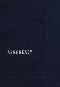 Tessuto blu navy con una finitura strutturata; presenta "AEROREADY" in testo bianco. Include un dettaglio di cucitura per una maggiore struttura.