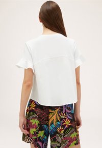 Haut blanc à manches courtes avec des poignets froncés, assorti à un short noir à motif floral coloré. Tissu doux et coupe décontractée.