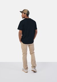 Černé bavlněné tričko, uvolněný střih, v kombinaci s béžovými chinos kalhotami a bílými teniskami, doplněné dvoubarevnou čepicí s zakřiveným okrajem.